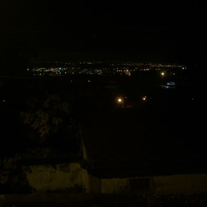 Close to the break of dawn, many birds can be heard singing. The city lights are visible in the distance.